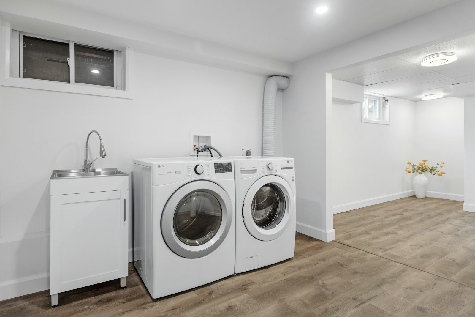 A bright, finished basement laundry room with white walls, a utility sink, and a washer and dryer