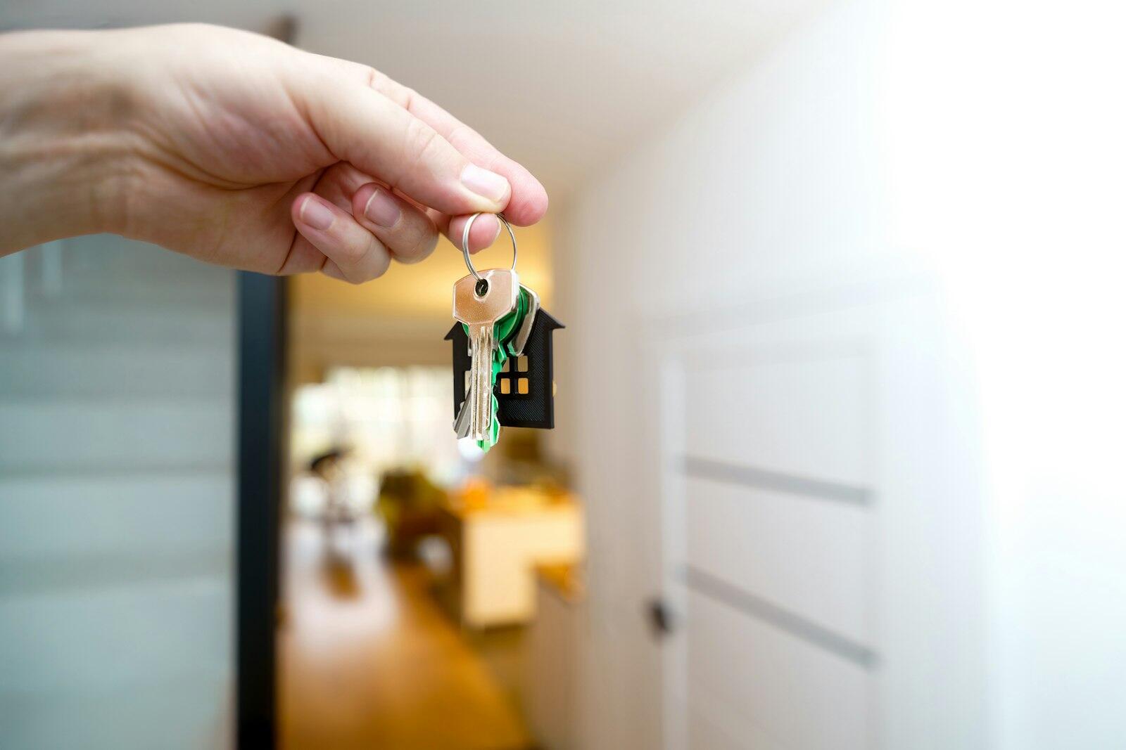 A hand holding a set of house keys with a blurred home interior in the background