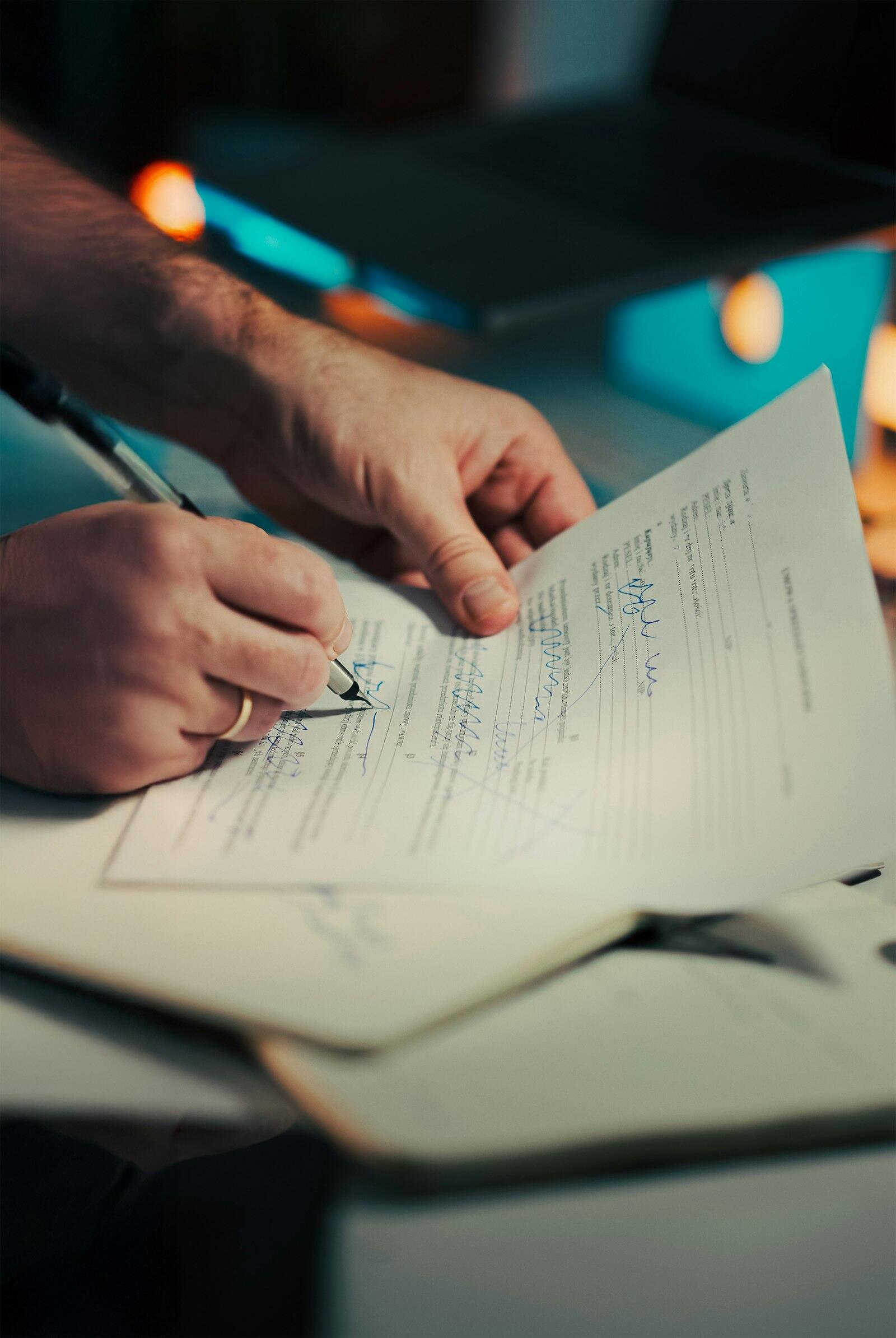 A close-up of hands signing a document with a pen on a desk